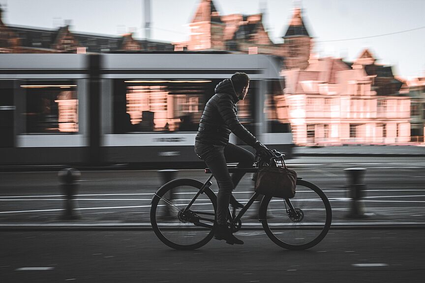 Mann geschäftlich auf Fahrrad, im Hintergrund fahrende Straßenbahn