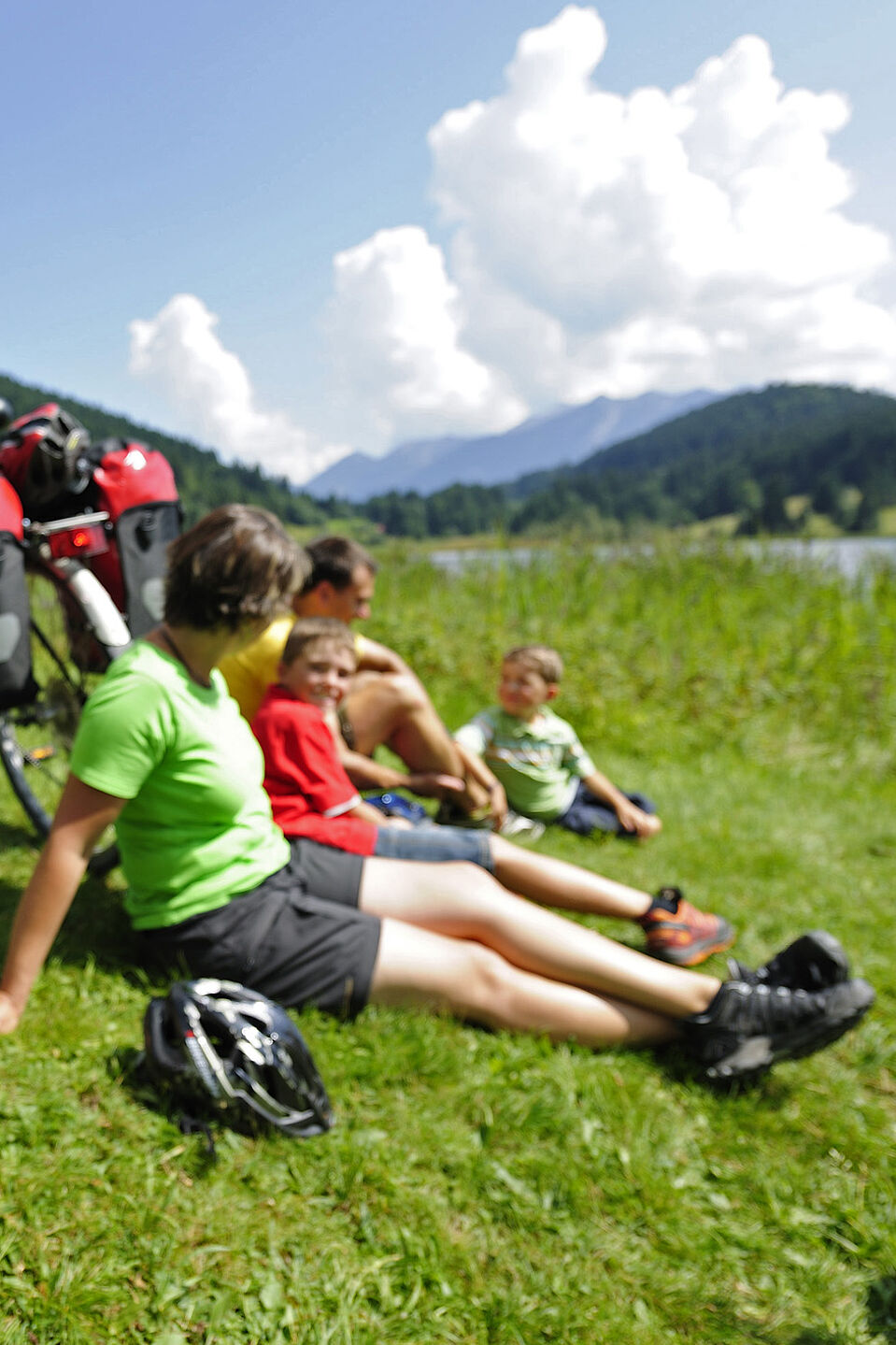 Trinkpause auf dem Radfernweg Familie mit Kindern sitzt am Seeufer im Gras.