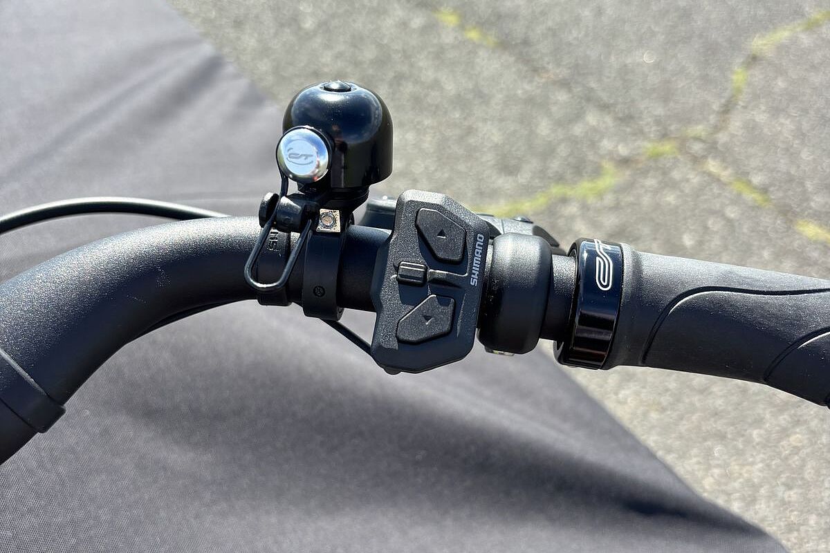 Ein Fahrradlenker mit einer kleinen schwarzen Klingel und zwei Tasten zur Bedienung des E‑Bikes.